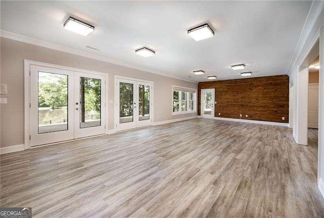 unfurnished living room with french doors, ornamental molding, and light wood-type flooring