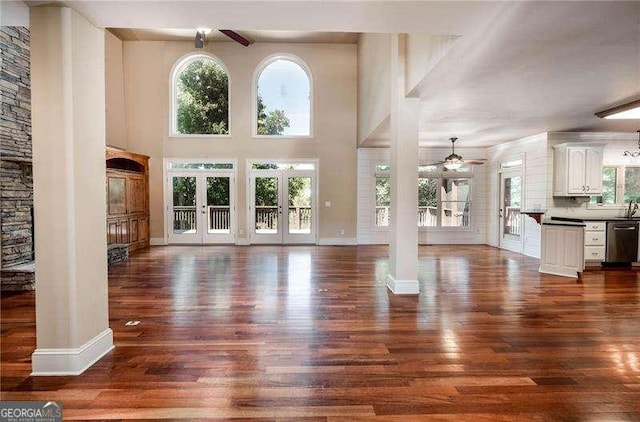 unfurnished living room featuring ornate columns, a healthy amount of sunlight, and dark wood-type flooring