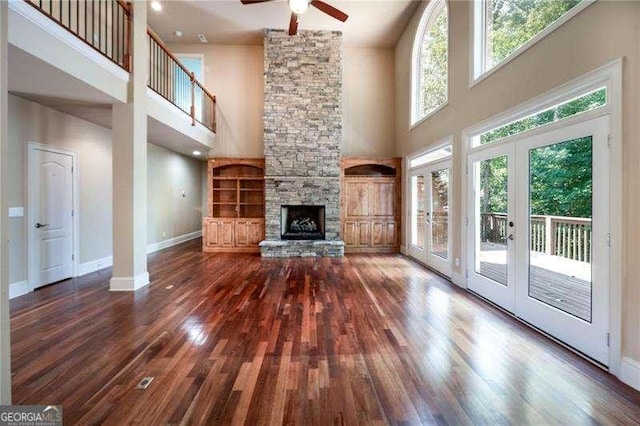 unfurnished living room featuring dark hardwood / wood-style flooring, a stone fireplace, french doors, and ceiling fan