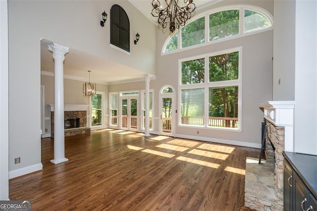 unfurnished living room with ornate columns, crown molding, a stone fireplace, and a notable chandelier