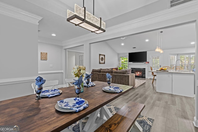 dining area with sink, crown molding, vaulted ceiling, and light wood-type flooring