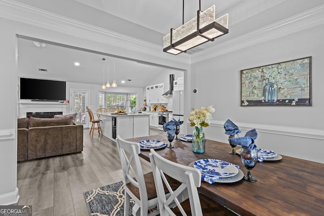 dining room featuring vaulted ceiling, crown molding, sink, and light hardwood / wood-style flooring