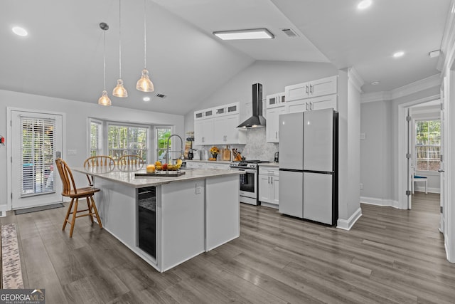 kitchen featuring wall chimney exhaust hood, stainless steel gas range, white cabinetry, a center island with sink, and fridge