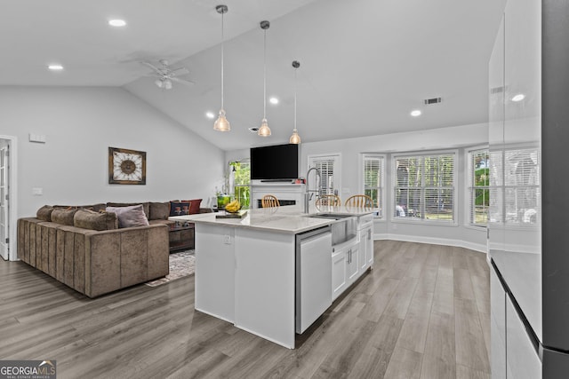 kitchen featuring white cabinetry, hanging light fixtures, a center island with sink, stainless steel dishwasher, and light hardwood / wood-style floors