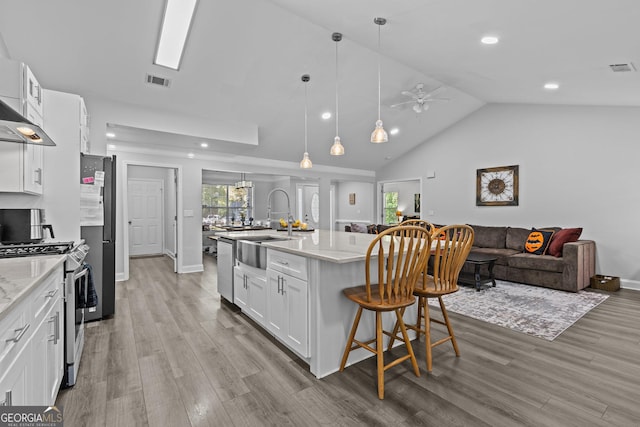 kitchen featuring appliances with stainless steel finishes, a kitchen island with sink, white cabinets, and light stone counters