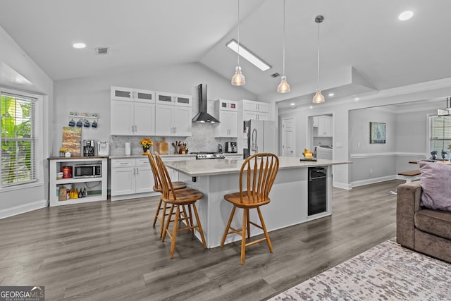 kitchen with appliances with stainless steel finishes, a breakfast bar, pendant lighting, white cabinetry, and wall chimney exhaust hood