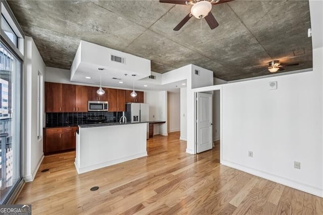 kitchen featuring appliances with stainless steel finishes, decorative light fixtures, decorative backsplash, a kitchen island with sink, and light wood-type flooring