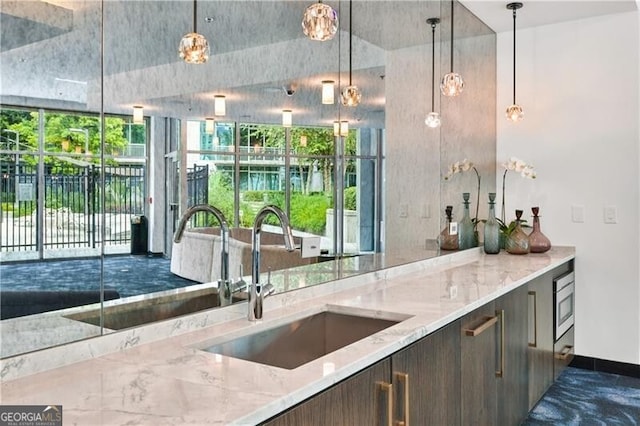 kitchen featuring light stone counters, sink, dark brown cabinetry, and hanging light fixtures