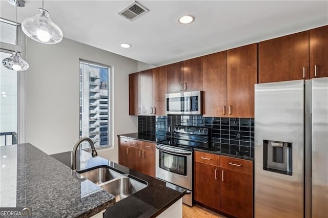 kitchen featuring sink, hanging light fixtures, dark stone countertops, stainless steel appliances, and backsplash