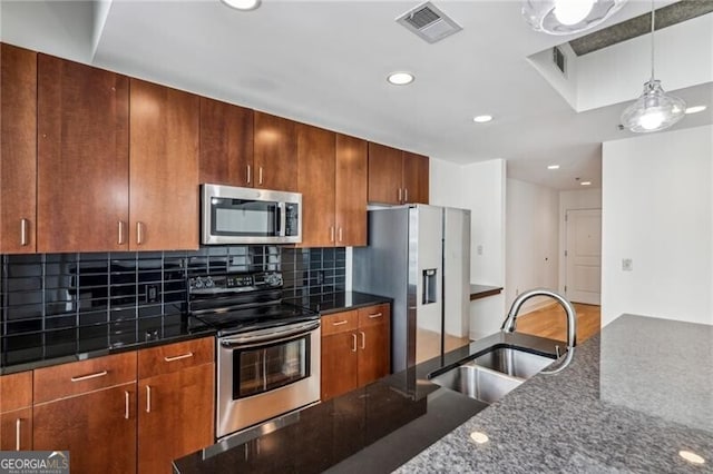 kitchen featuring sink, appliances with stainless steel finishes, pendant lighting, dark stone counters, and backsplash