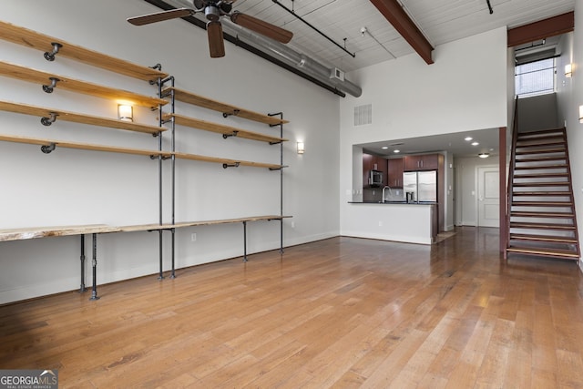 unfurnished living room featuring beam ceiling, ceiling fan, a high ceiling, and light wood-type flooring