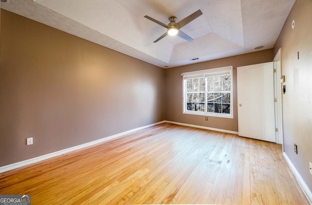 spare room with a tray ceiling, light hardwood / wood-style flooring, a textured ceiling, and ceiling fan