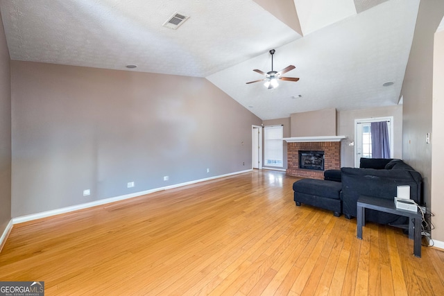 unfurnished living room featuring vaulted ceiling, a fireplace, ceiling fan, light hardwood / wood-style floors, and a textured ceiling