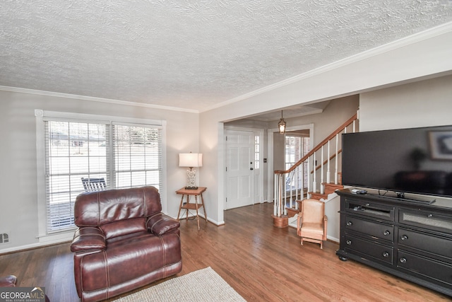 living area featuring crown molding, a textured ceiling, wood finished floors, baseboards, and stairs