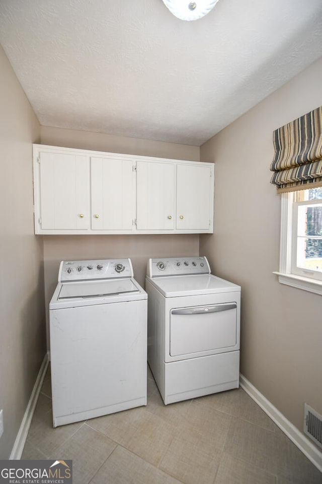 clothes washing area with washing machine and clothes dryer, cabinet space, visible vents, a textured ceiling, and baseboards