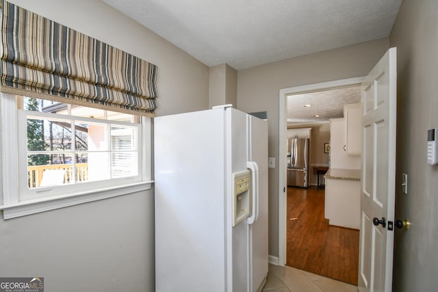 kitchen featuring white refrigerator with ice dispenser, light wood finished floors, white cabinetry, a textured ceiling, and stainless steel fridge