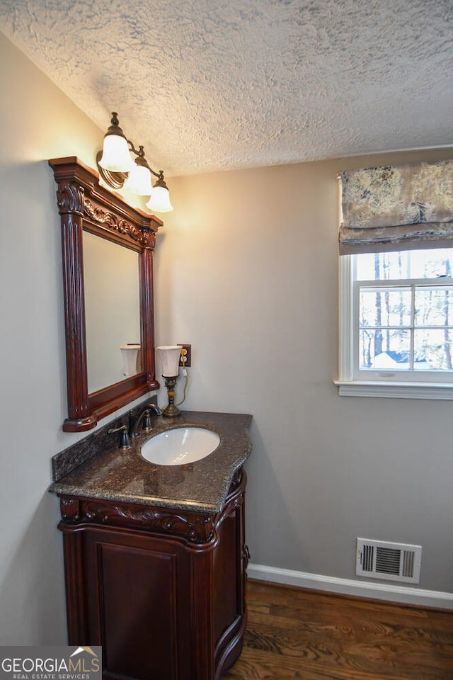 bathroom featuring a textured ceiling, wood finished floors, vanity, visible vents, and baseboards