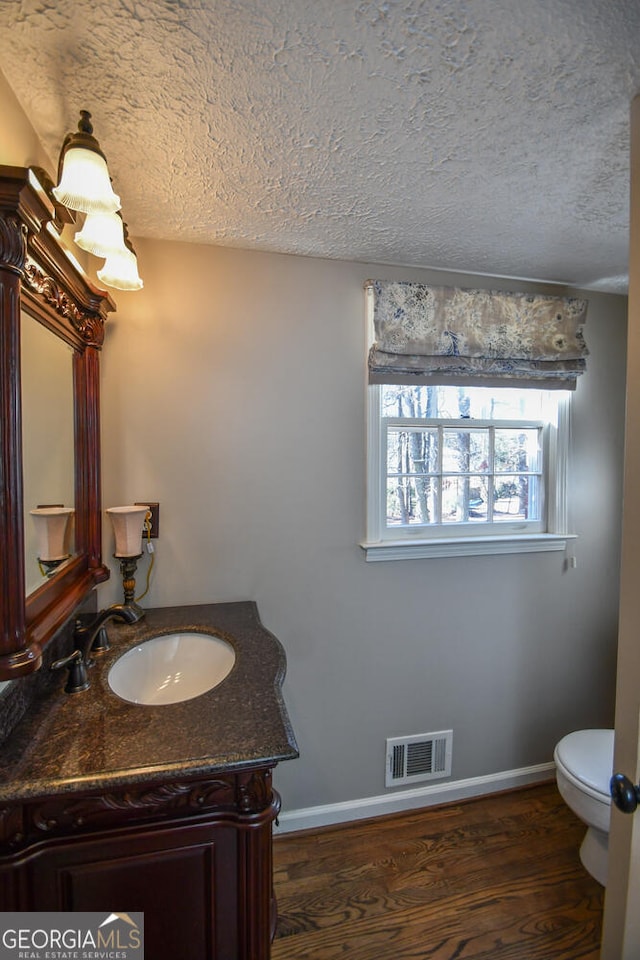 half bathroom featuring visible vents, toilet, wood finished floors, a textured ceiling, and vanity