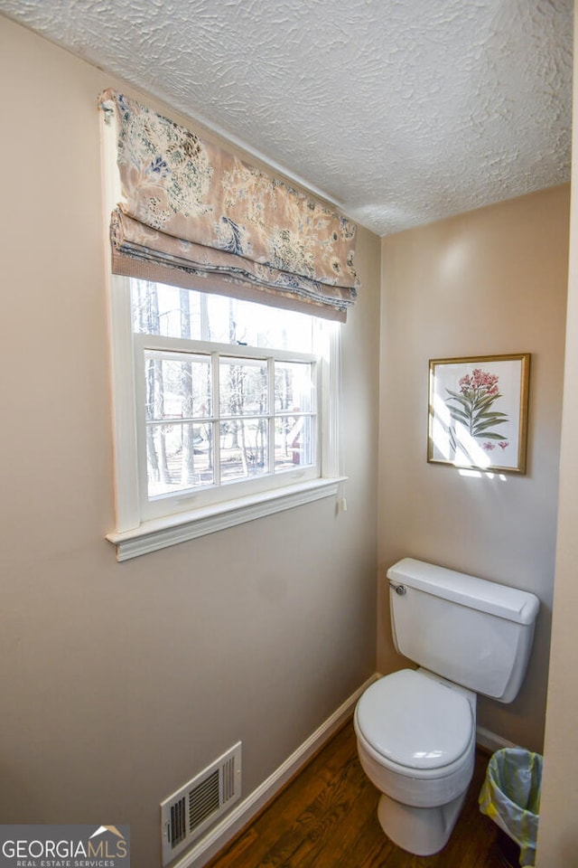 bathroom with a textured ceiling, toilet, wood finished floors, visible vents, and baseboards