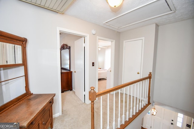 hall with attic access, light colored carpet, a textured ceiling, and an upstairs landing