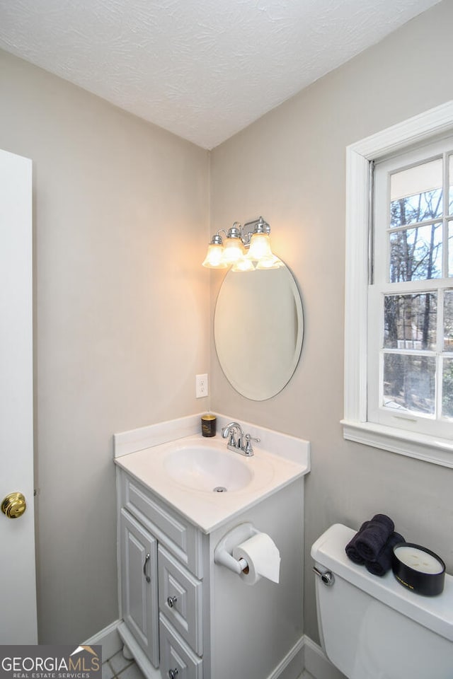 half bath with toilet, baseboards, a textured ceiling, and vanity