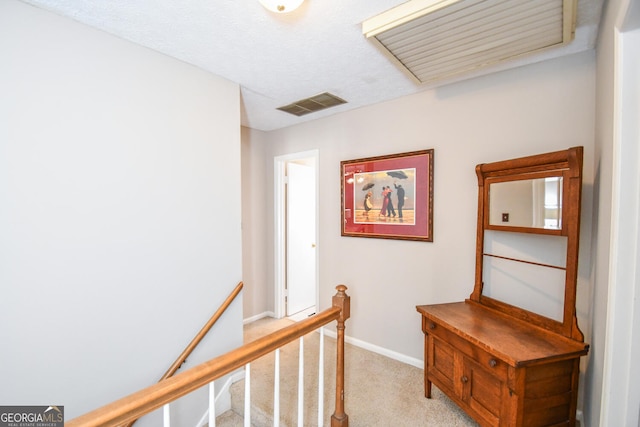 hall featuring a textured ceiling, light carpet, an upstairs landing, visible vents, and baseboards