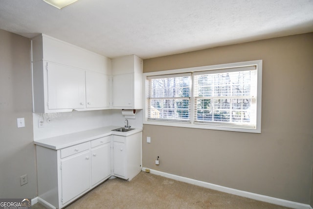 kitchen with light colored carpet, a sink, baseboards, white cabinets, and light countertops