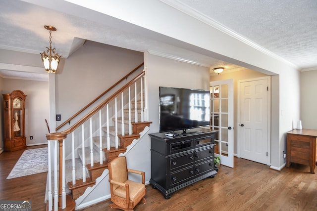 living room featuring crown molding, a textured ceiling, wood finished floors, baseboards, and stairs