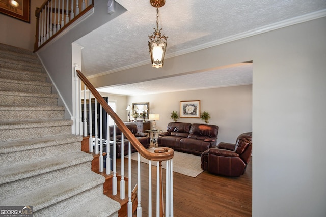 stairs with a textured ceiling, ornamental molding, and wood finished floors