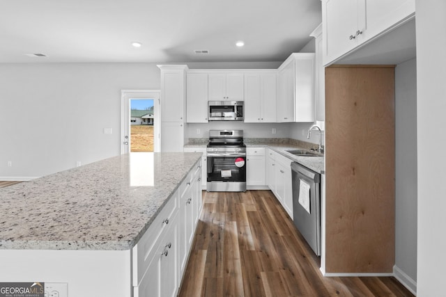 kitchen with a kitchen island, appliances with stainless steel finishes, white cabinetry, sink, and light stone countertops