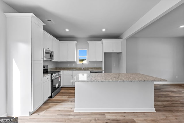 kitchen featuring white cabinetry, a center island, stainless steel appliances, light stone countertops, and light hardwood / wood-style flooring