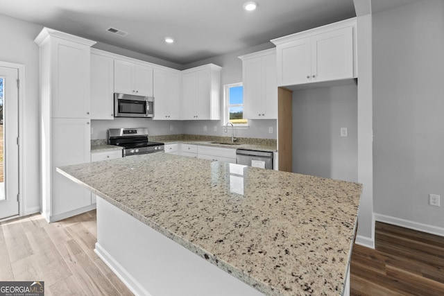 kitchen featuring sink, light stone counters, appliances with stainless steel finishes, a kitchen island, and white cabinets