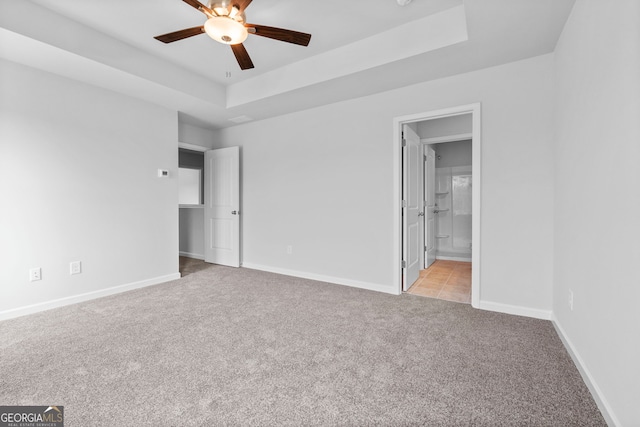 unfurnished bedroom featuring connected bathroom, a tray ceiling, light colored carpet, and ceiling fan