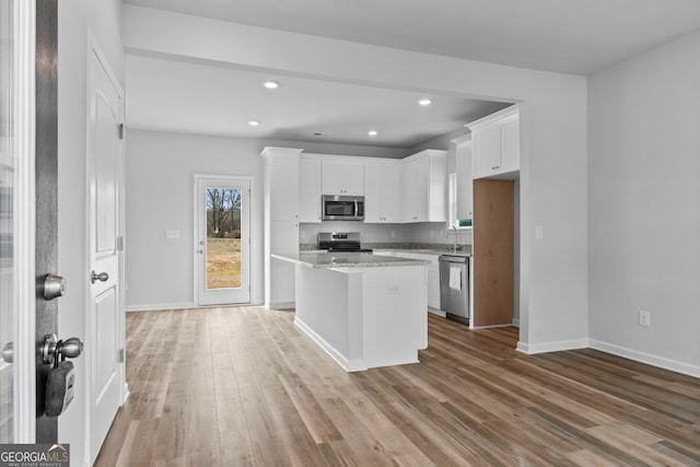 kitchen with stainless steel appliances, white cabinetry, light stone countertops, and a center island