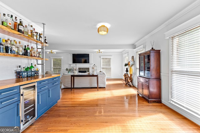 bar with blue cabinets, wine cooler, ornamental molding, plenty of natural light, and light wood-type flooring