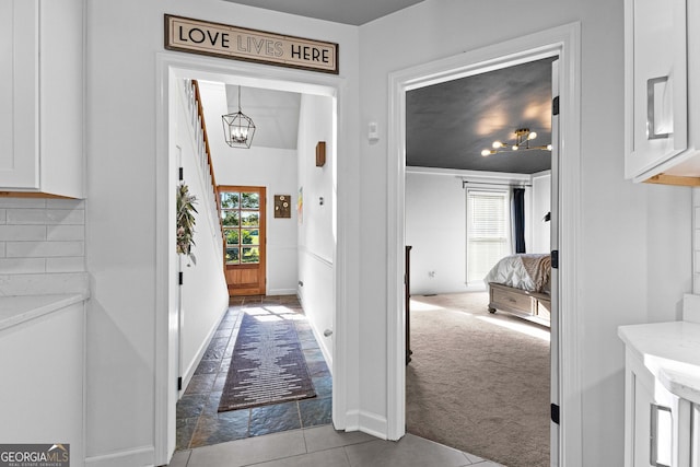 hallway with a healthy amount of sunlight, light colored carpet, and an inviting chandelier