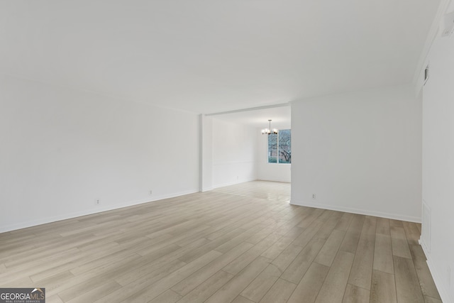 empty room featuring light wood-type flooring and a chandelier