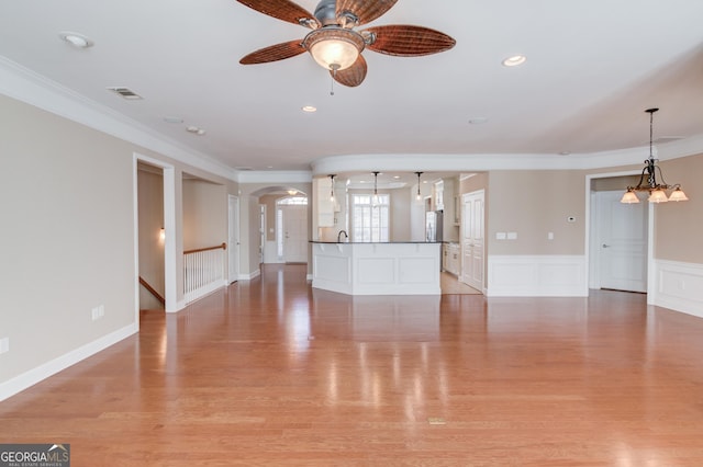 unfurnished living room with crown molding, ceiling fan with notable chandelier, and light wood-type flooring