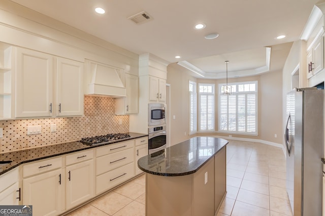 kitchen with a kitchen island, appliances with stainless steel finishes, dark stone counters, a raised ceiling, and custom range hood