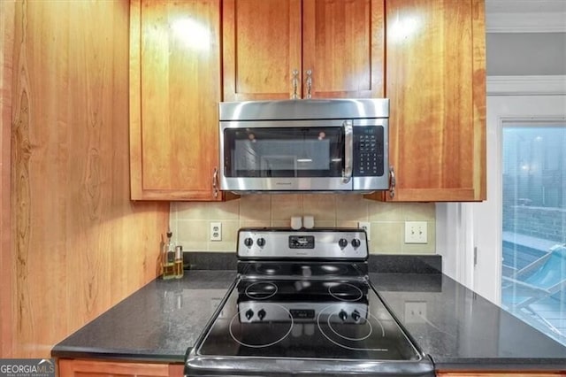 kitchen featuring stainless steel appliances, ornamental molding, dark stone countertops, and backsplash