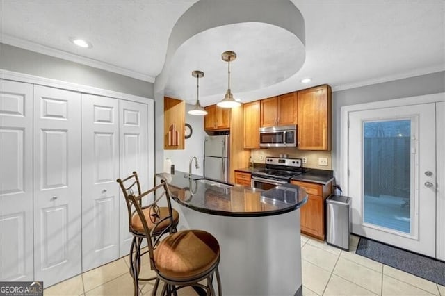 kitchen with light tile patterned flooring, a breakfast bar area, hanging light fixtures, ornamental molding, and stainless steel appliances