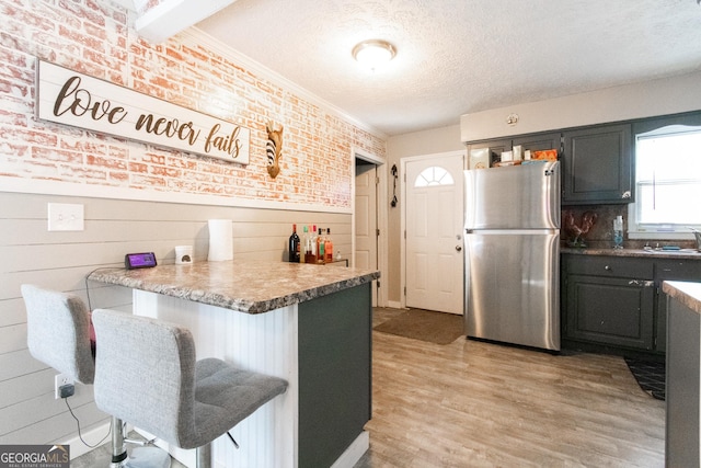 kitchen featuring a breakfast bar area, light hardwood / wood-style flooring, a textured ceiling, stainless steel refrigerator, and kitchen peninsula