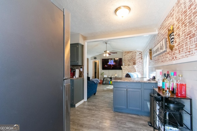 kitchen with brick wall, hardwood / wood-style floors, lofted ceiling, ceiling fan, and a textured ceiling