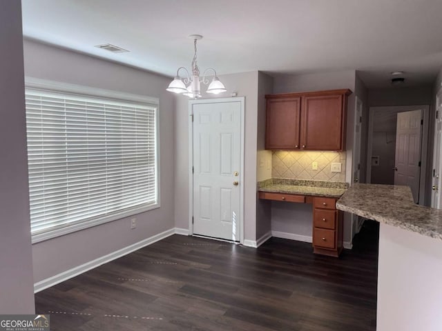 kitchen featuring dark wood-type flooring, an inviting chandelier, hanging light fixtures, built in desk, and decorative backsplash