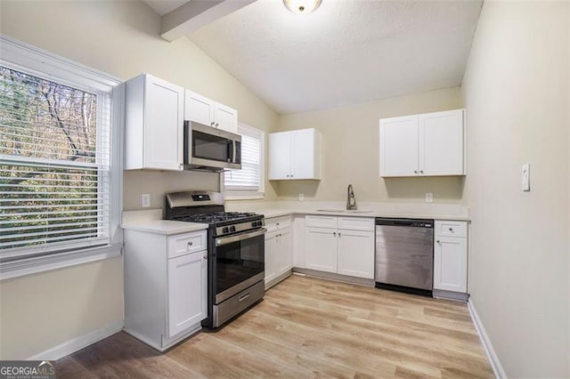 kitchen with sink, light hardwood / wood-style flooring, appliances with stainless steel finishes, white cabinetry, and lofted ceiling with beams