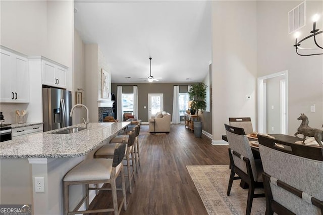 kitchen featuring stainless steel fridge, visible vents, a stone fireplace, white cabinetry, and a sink