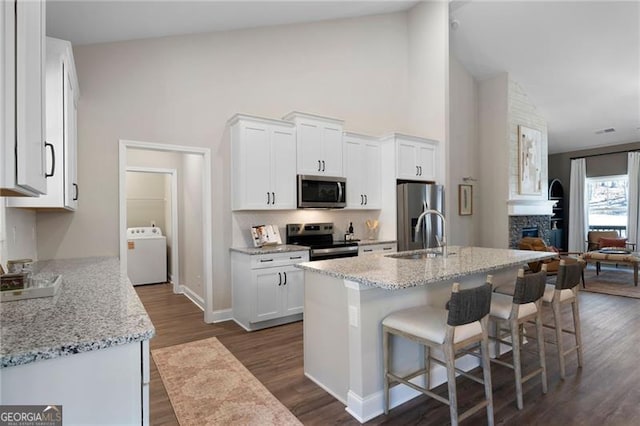 kitchen with a breakfast bar, stainless steel appliances, white cabinets, a sink, and washer / dryer