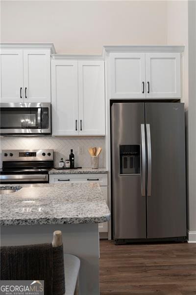 kitchen featuring dark wood finished floors, stainless steel appliances, tasteful backsplash, white cabinets, and light stone countertops