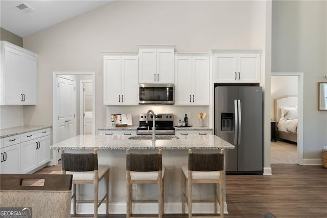 kitchen featuring appliances with stainless steel finishes, white cabinetry, an island with sink, and light stone countertops