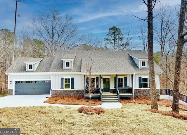 view of front of house featuring a shingled roof, stone siding, an attached garage, covered porch, and board and batten siding